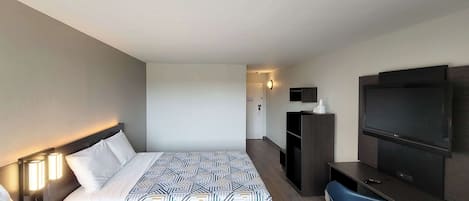 A hotel room with two beds, a desk, a chair, a TV, and a minibar.