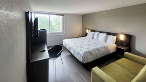 A modern hotel room with a bed, a desk with a chair, a television, and a window with a view of trees. - Motel 6 Jackson, TN (Jackson)