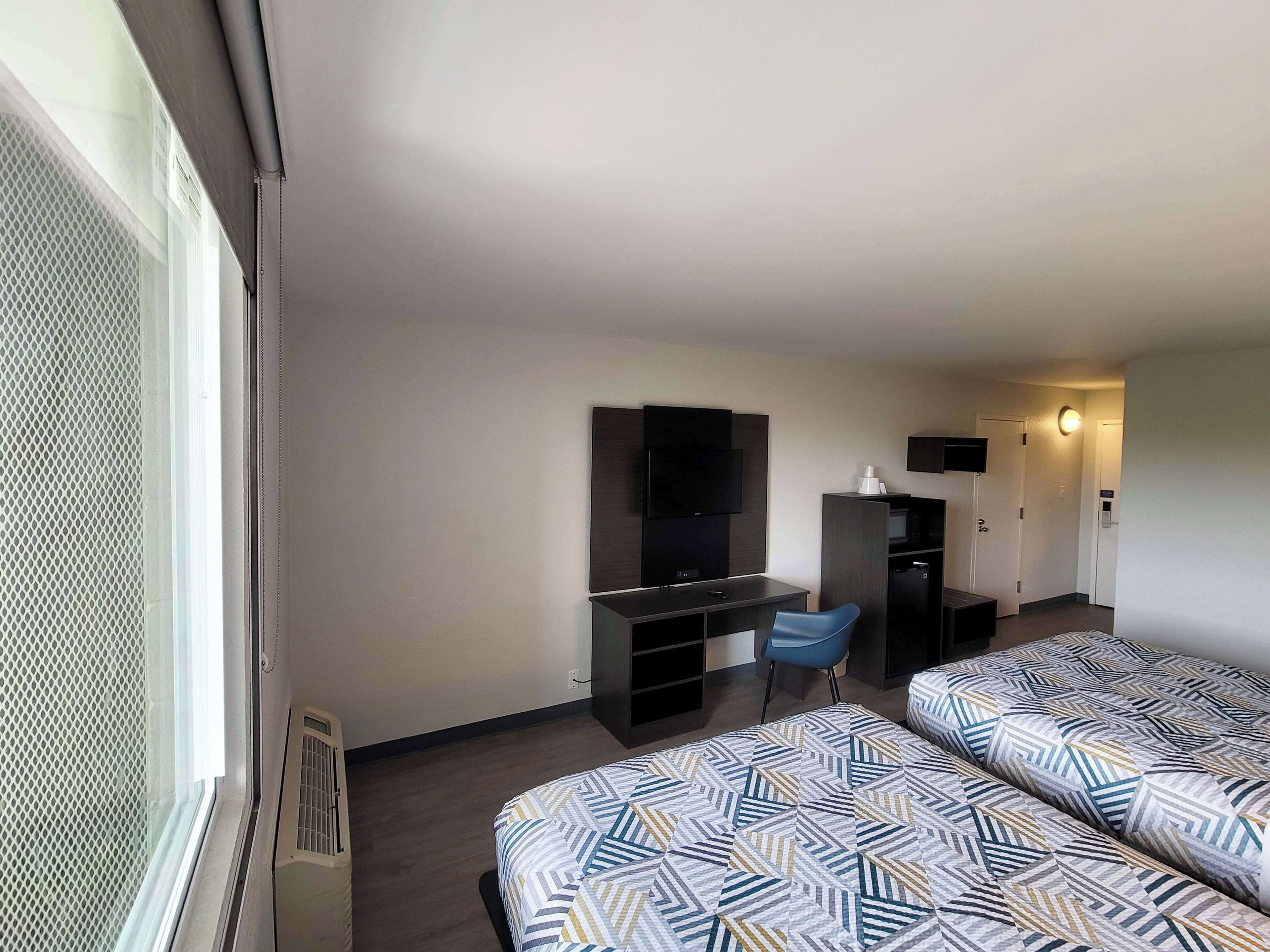 A hotel room with two beds, a desk, a chair, a TV, and a minibar.