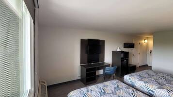 A hotel room with two beds, a desk, a chair, a TV, and a minibar.