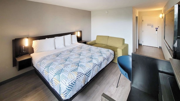 A hotel room with a bed, a sofa, a desk, and a TV. - Motel 6 Jackson, TN (Jackson)