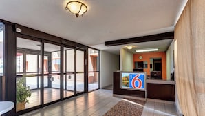A hotel lobby with a reception desk, a large glass door entrance, and a clock on the wall. - Motel 6 Jackson, TN (Jackson)