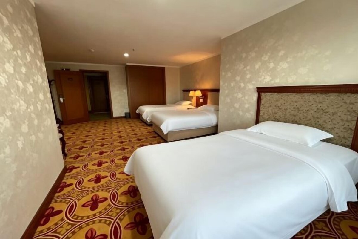 A hotel room with two beds, a patterned carpet, and a door leading to another room.