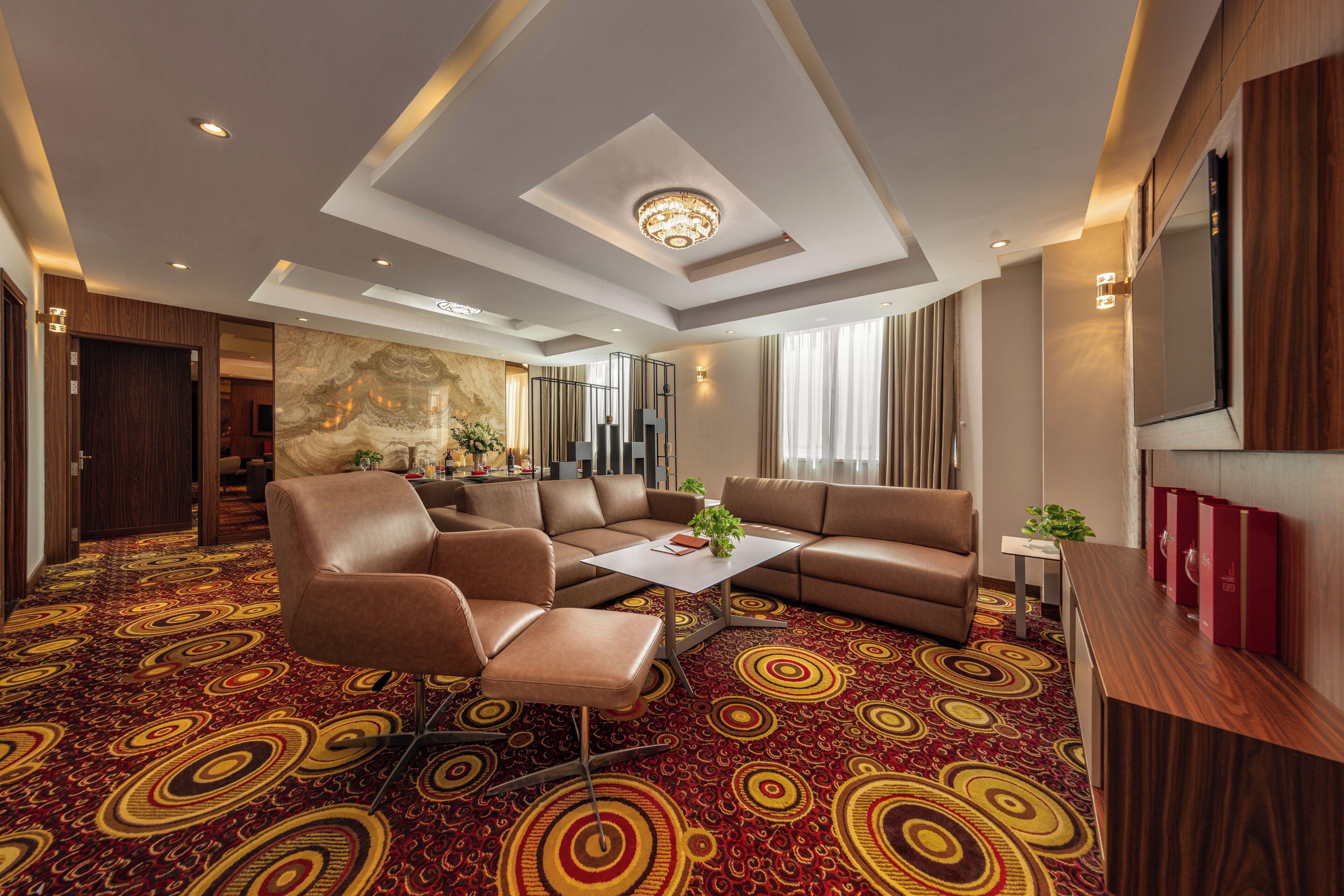 A hotel room with a large sofa, a coffee table, a TV, and a patterned carpet.