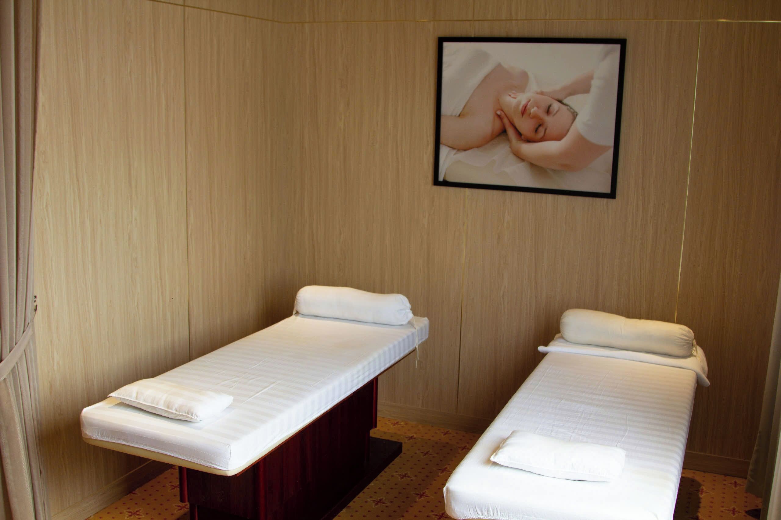 Two single beds with white linens and pillows, a wooden wall, and a framed picture of a person receiving a massage.