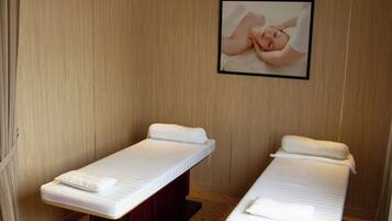Two single beds with white linens and pillows, a wooden wall, and a framed picture of a person receiving a massage.