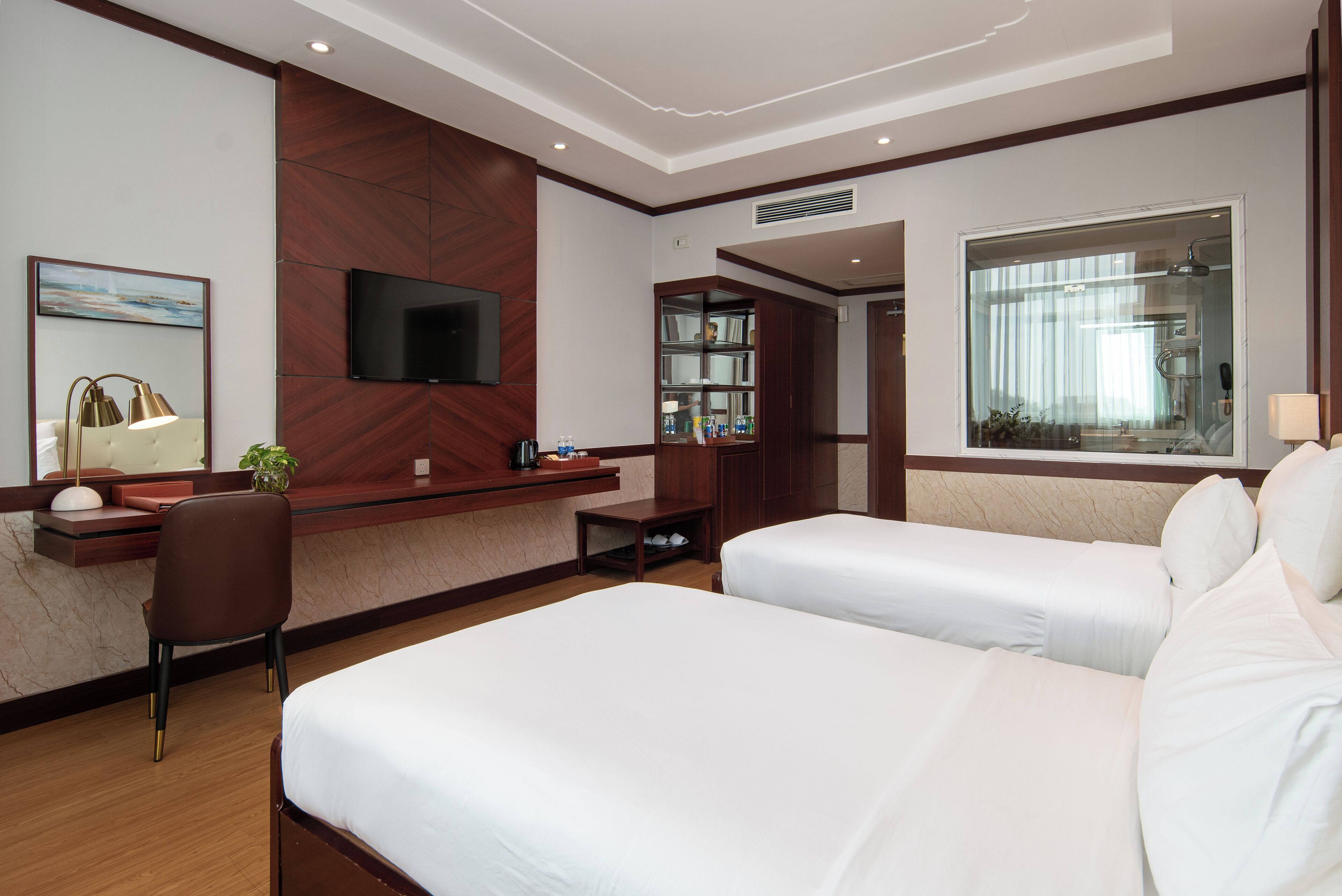 Une chambre d’hôtel avec deux lits, un téléviseur fixé au mur, un bureau avec une chaise et une fenêtre avec des rideaux.