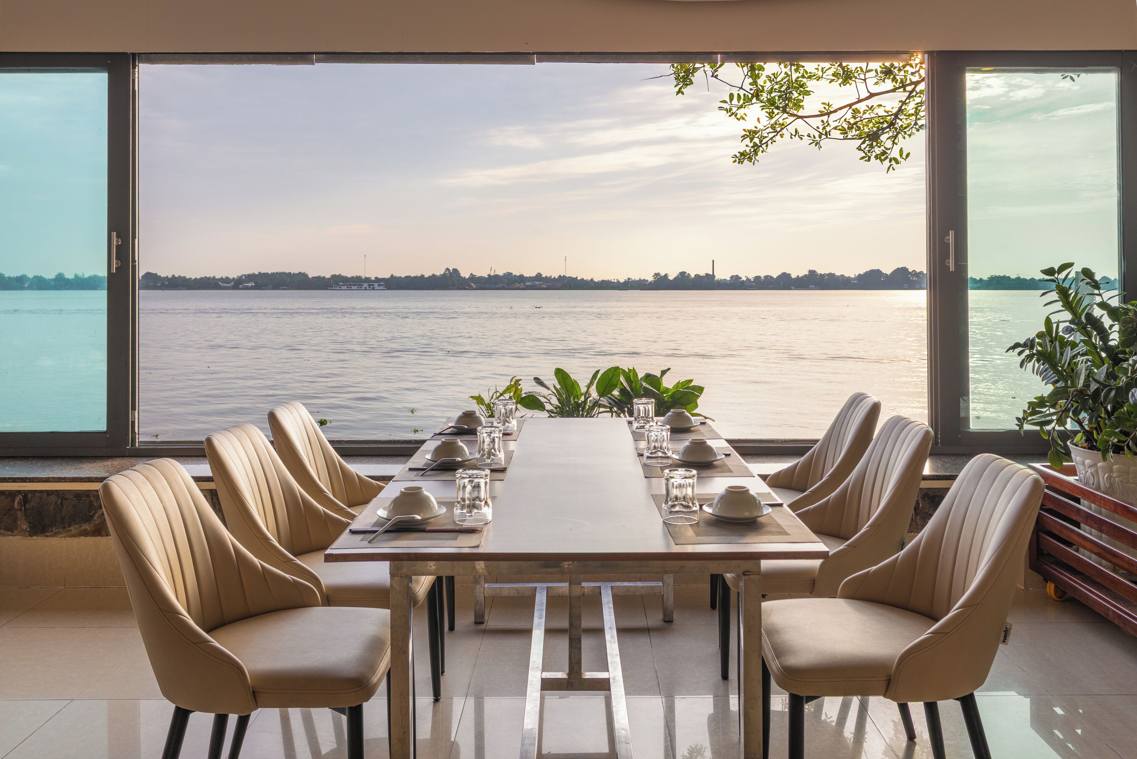 A dining table with six chairs, set for a meal, overlooking a body of water with a distant shoreline.