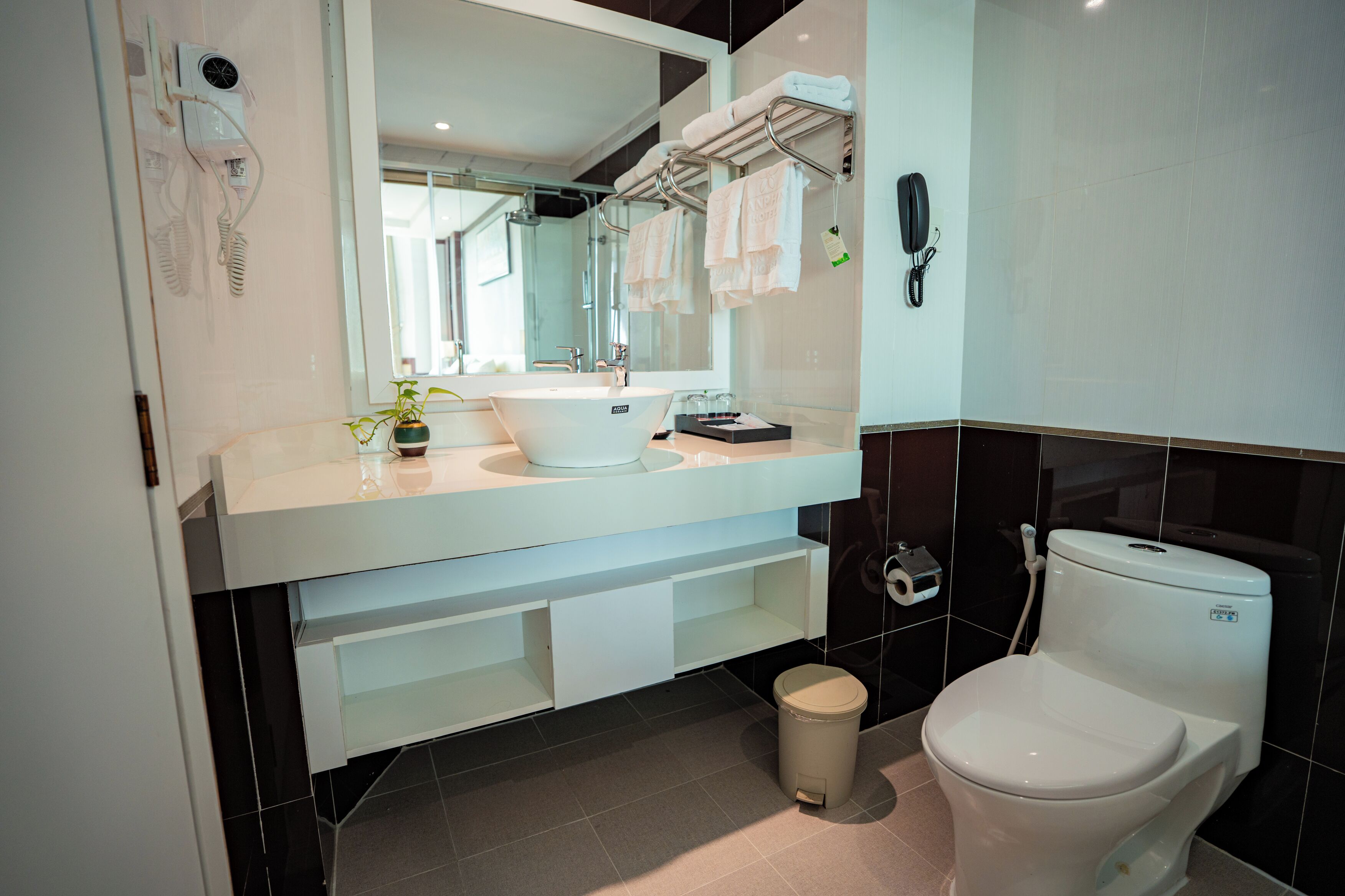 Casa de banho moderna com lavatório branco, espelho e sanita. Toalhas penduradas num porta-toalhas e um cesto de lixo.