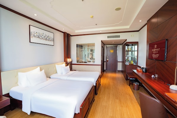 A hotel room with two beds, a wooden desk, a mirror, and a TV.