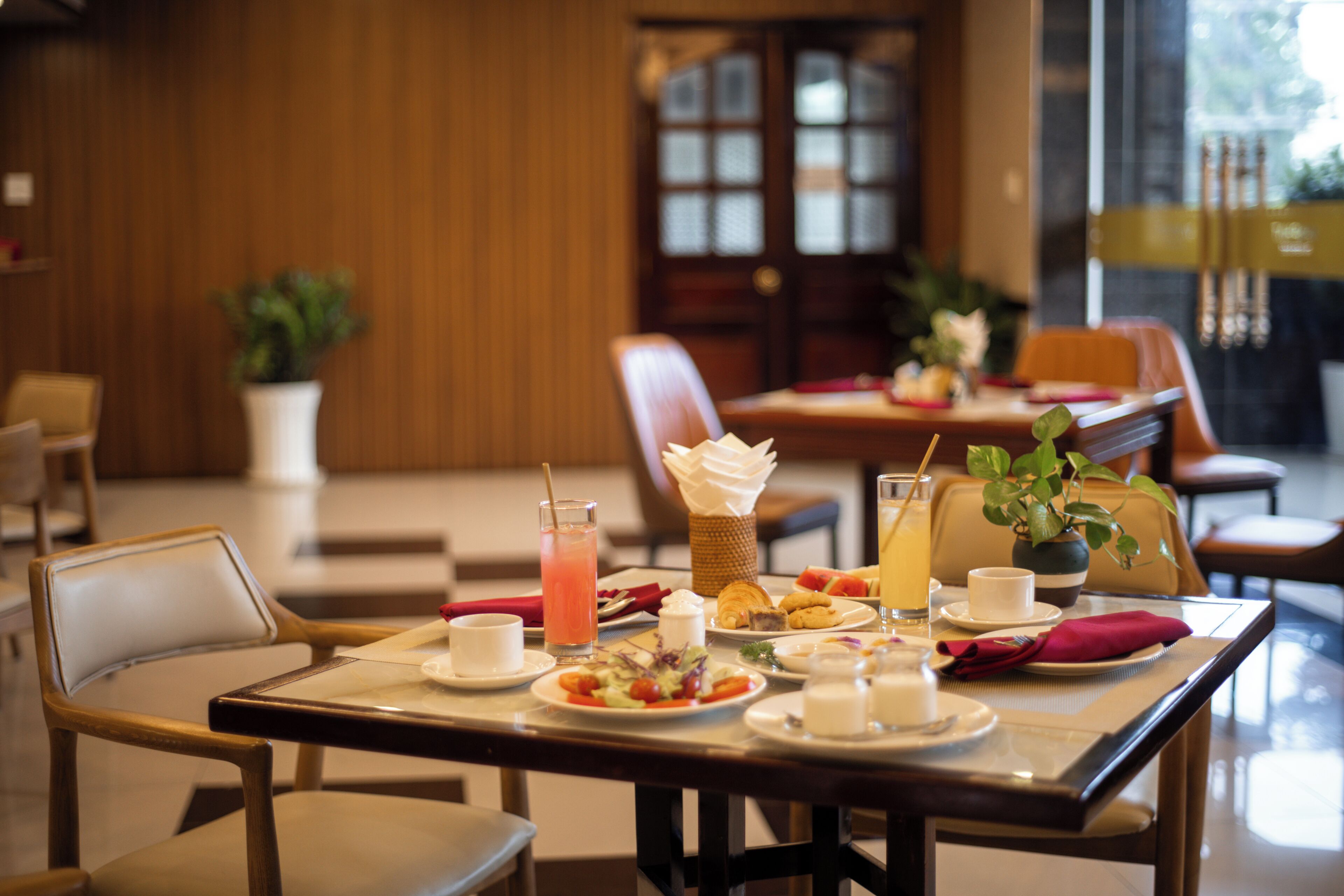 Un coin repas avec une table dressée pour deux personnes, comprenant des assiettes de nourriture, un verre de jus de fruits et une carafe d’eau.