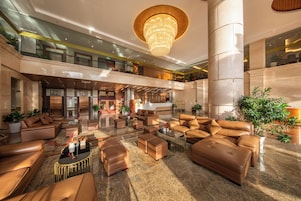 A spacious lobby with leather sofas, a chandelier, and a high ceiling.