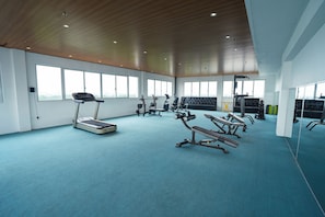 A spacious gym with a blue carpet, treadmills, weight machines, and large windows allowing natural light. - Van Phat Riverside Hotel (Can Tho)