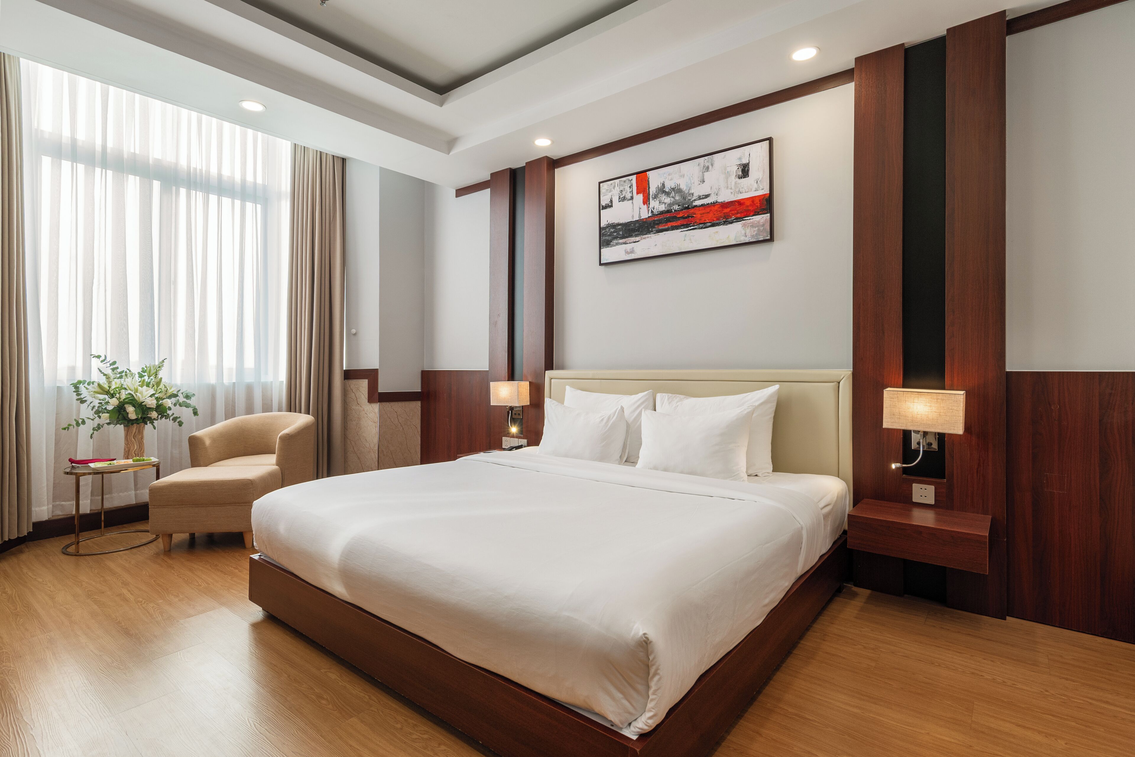 A hotel room with a large bed, a chair, a bedside table with a lamp, and a painting on the wall.