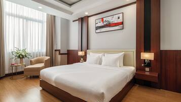 A hotel room with a large bed, a chair, a bedside table with a lamp, and a painting on the wall.