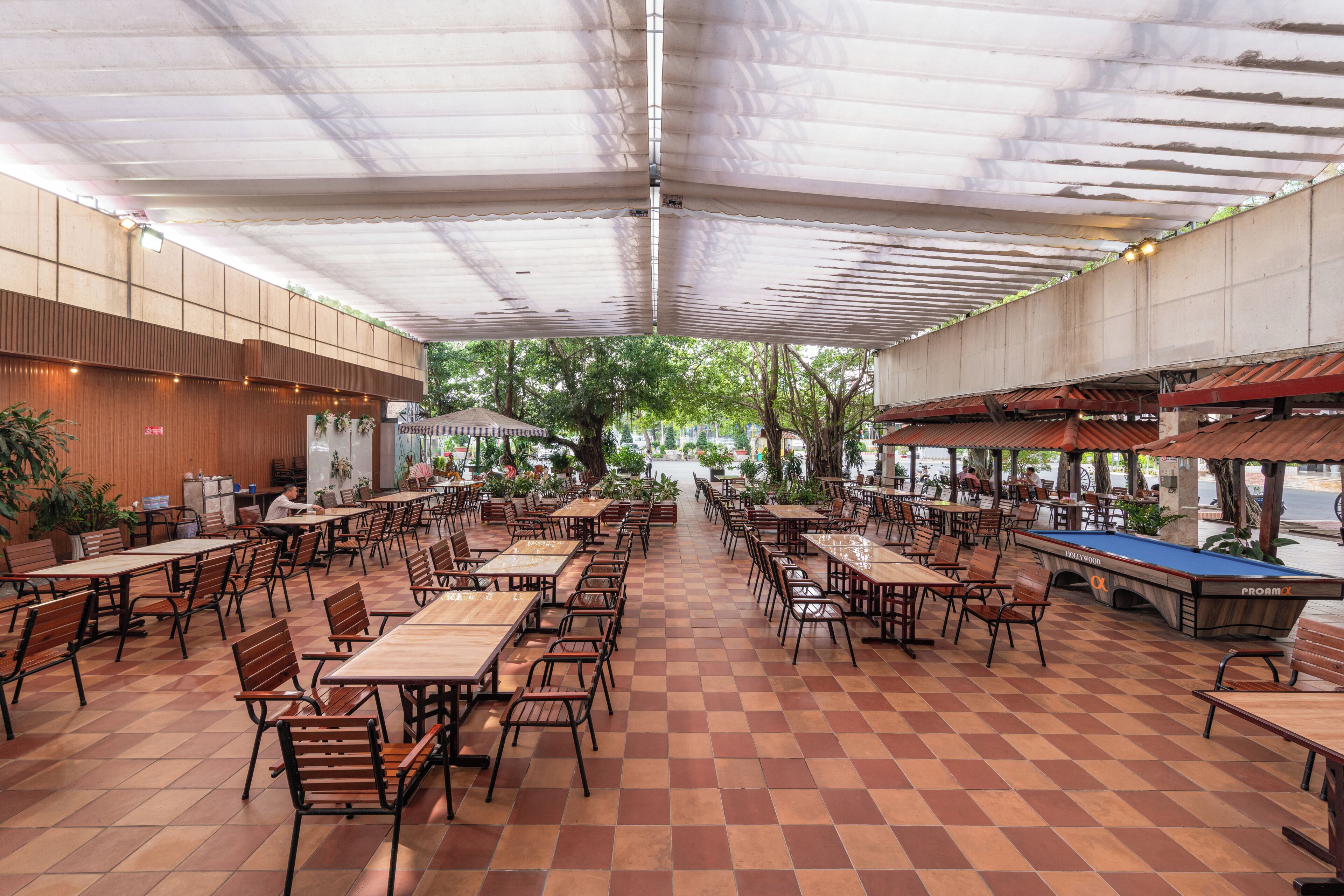 Un café al aire libre con varias mesas y sillas, una mesa de billar y un paseo techado.