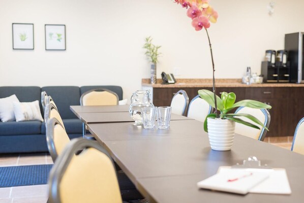 Meetings take place around a long, dark brown table, surrounded by cream-colored chairs and a potted orchid.