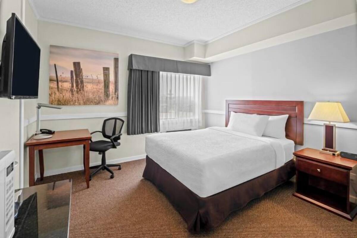 Une chambre d’hôtel avec un lit, un bureau, une chaise, une télévision, une lampe et une fenêtre avec des rideaux.
