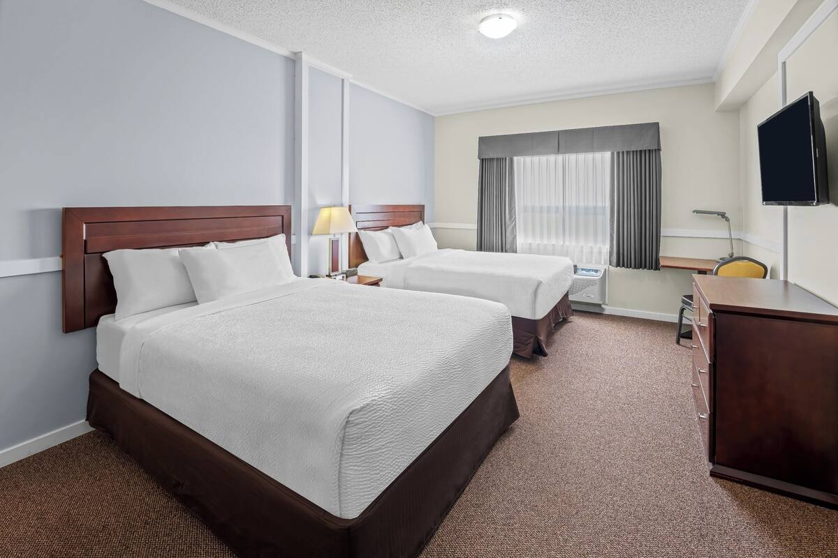 Une chambre d’hôtel avec deux lits, un bureau, une télévision et une fenêtre avec des rideaux.