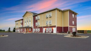 A multi-story hotel with a flat roof, a parking lot, and a small landscaped area.
