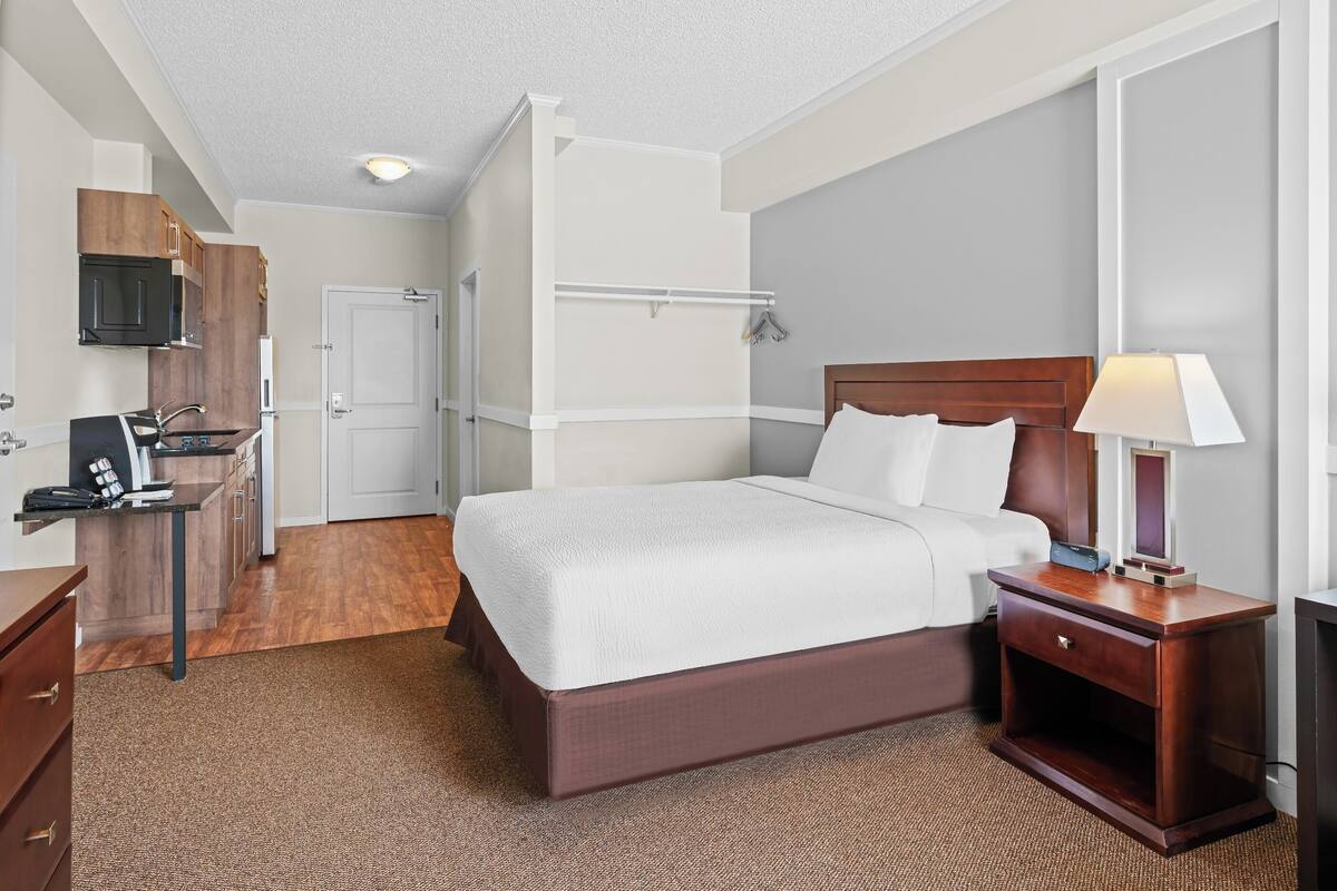 Une chambre d’hôtel comprenant un lit, une table de chevet, une lampe et un petit bureau avec un téléphone.