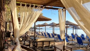 A beachside lounge with a dog lying on a cushioned bench, surrounded by umbrellas and beach chairs. - Villa Agape in Kala Nera Pelion (South Pelion)