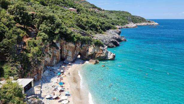 A coastal beach with clear turquoise waters, rocky cliffs, and a few buildings on the hillside. - Villa Agape in Kala Nera Pelion (South Pelion)