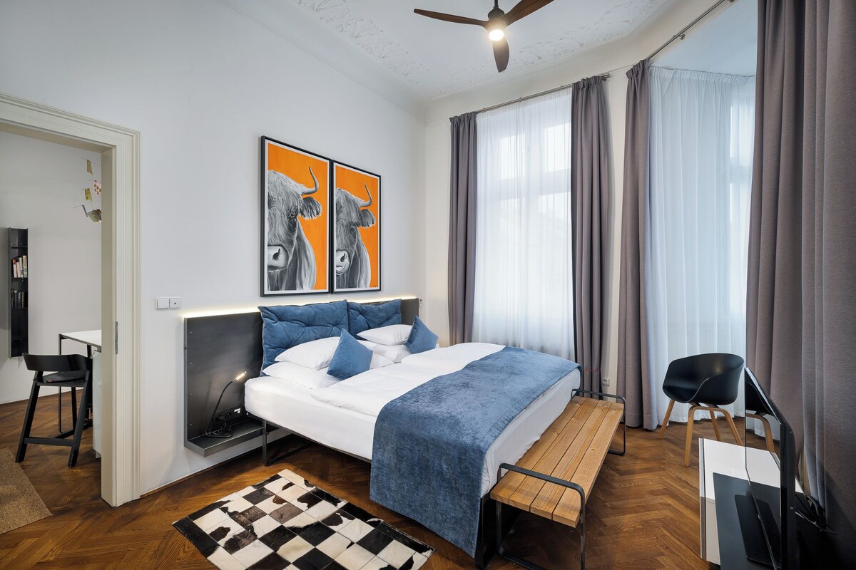 Un dormitorio moderno con cama, mesita de noche, silla y una obra de arte.