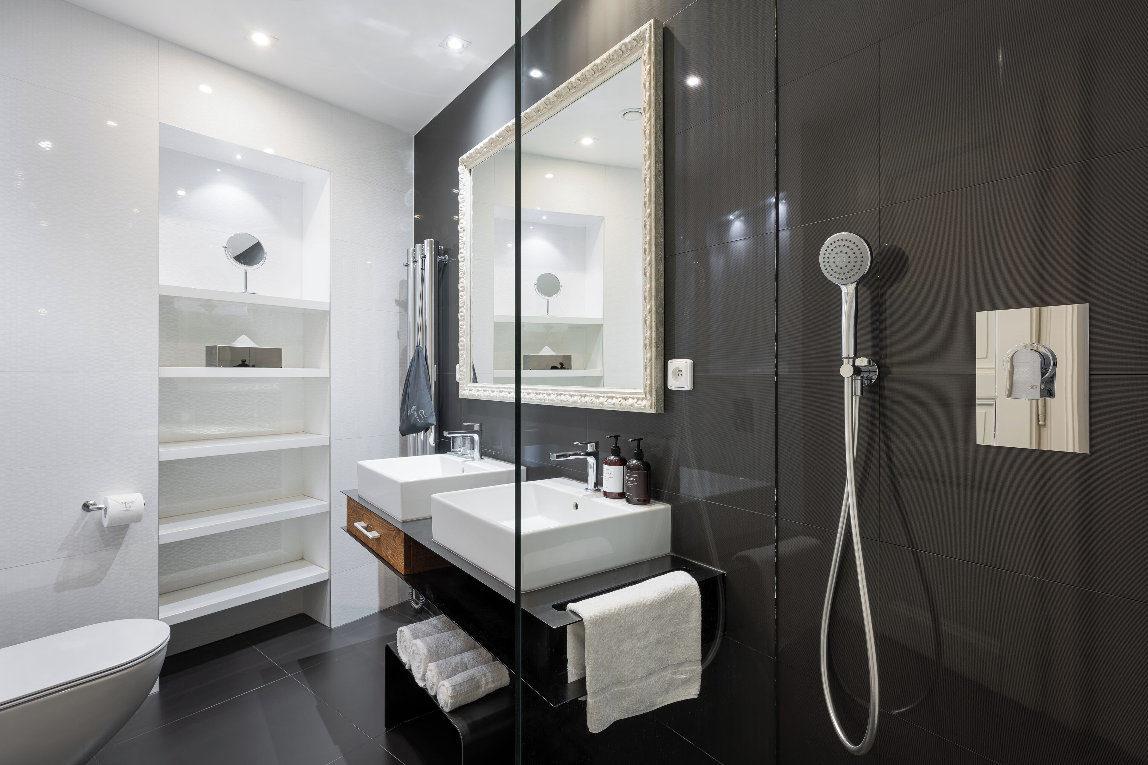 A modern bathroom with two sinks, a large mirror, a shower, and a toilet.