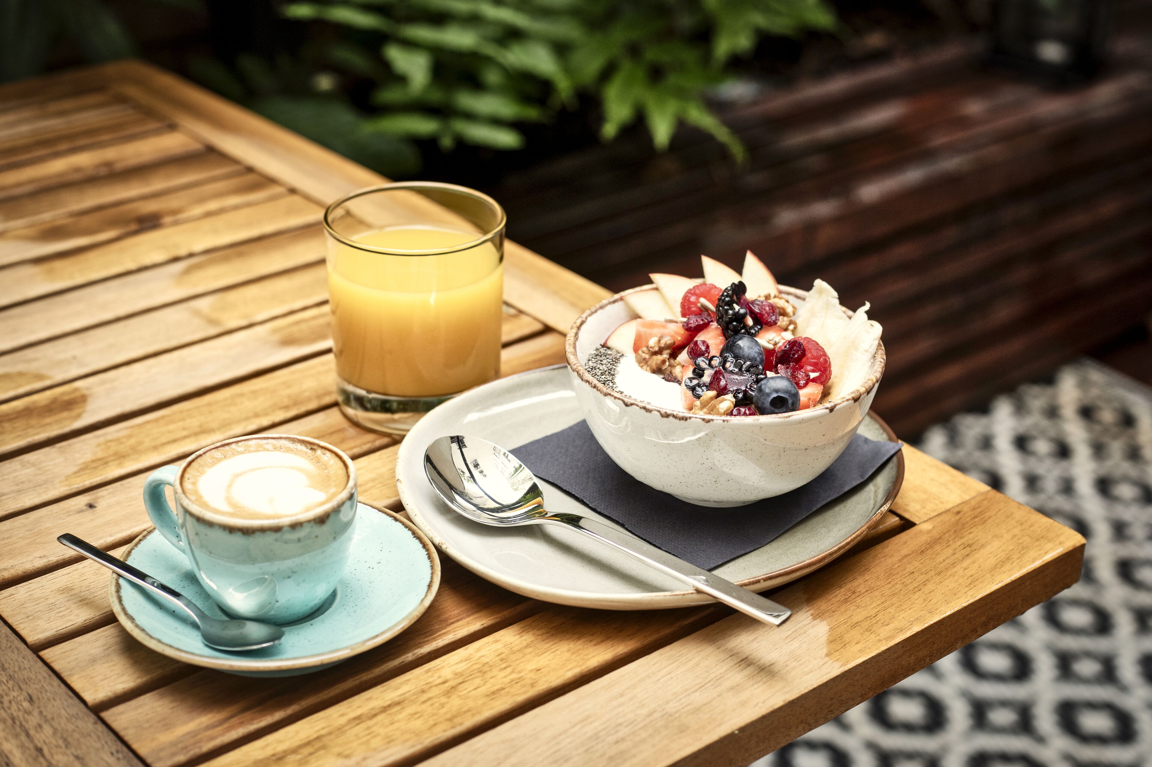 Una mesa de madera con una taza de café, un vaso de jugo de naranja y un tazón de ensalada de frutas.