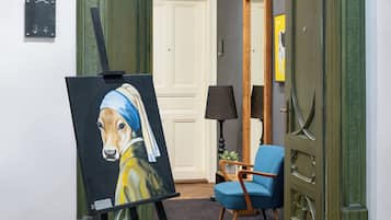 A room with a painting of a dog, a blue chair, a lamp, and a door.