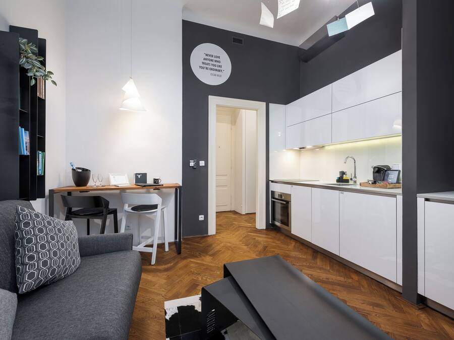Un appartement moderne avec un canapé gris, un coin repas et une cuisine dotée de meubles blancs.