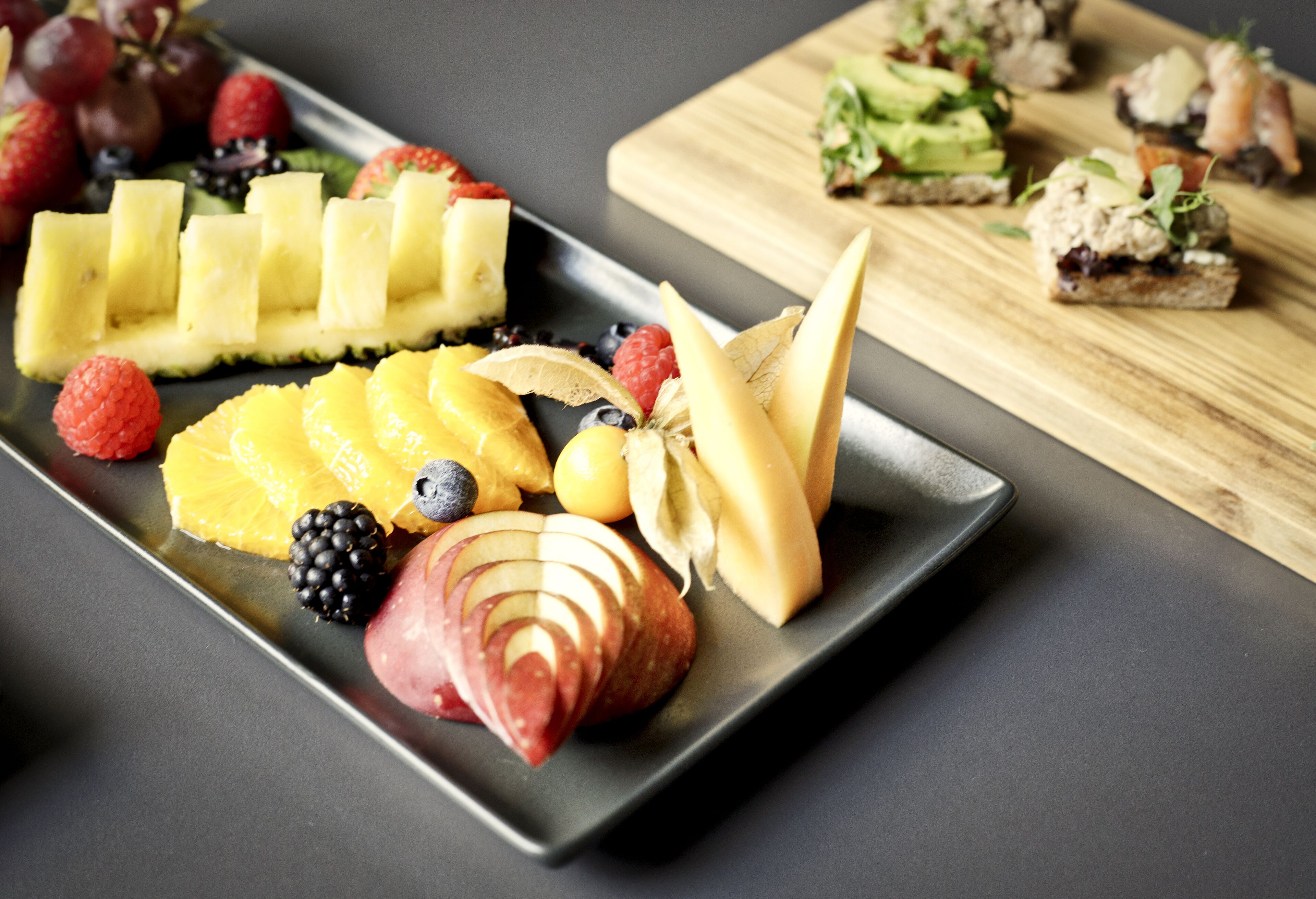 A fruit platter with sliced bananas, apples, oranges, and berries on a rectangular plate.