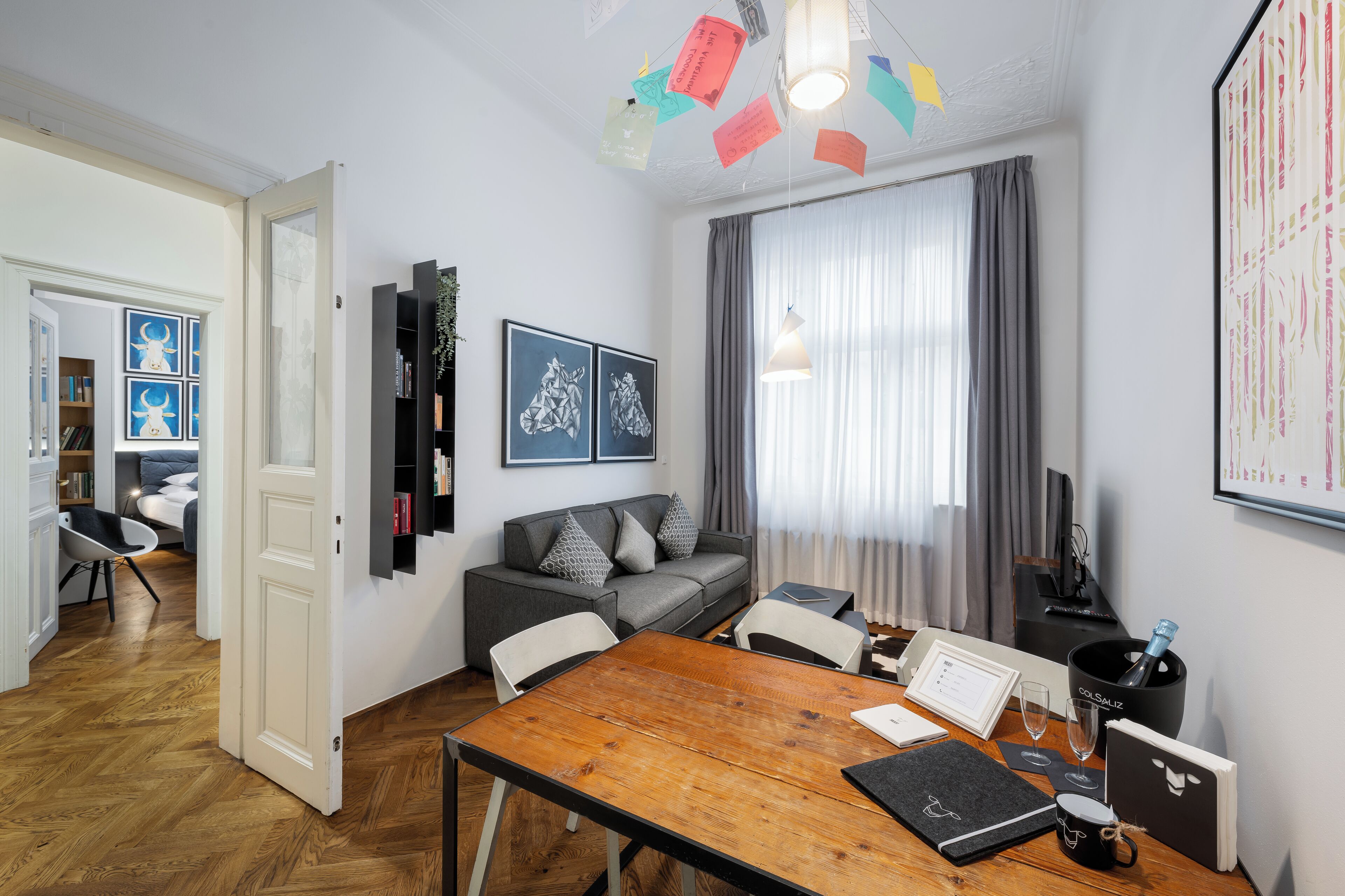Una sala de estar moderna con una mesa de comedor de madera, un sofá gris y un amplio ventanal con cortinas.