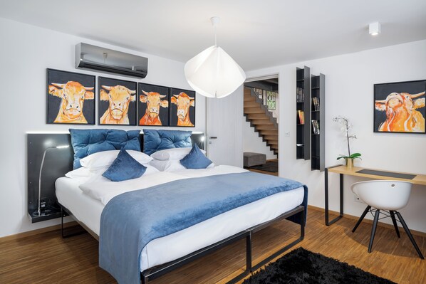 A modern bedroom with a bed, blue bedding, and artwork of cows on the wall.