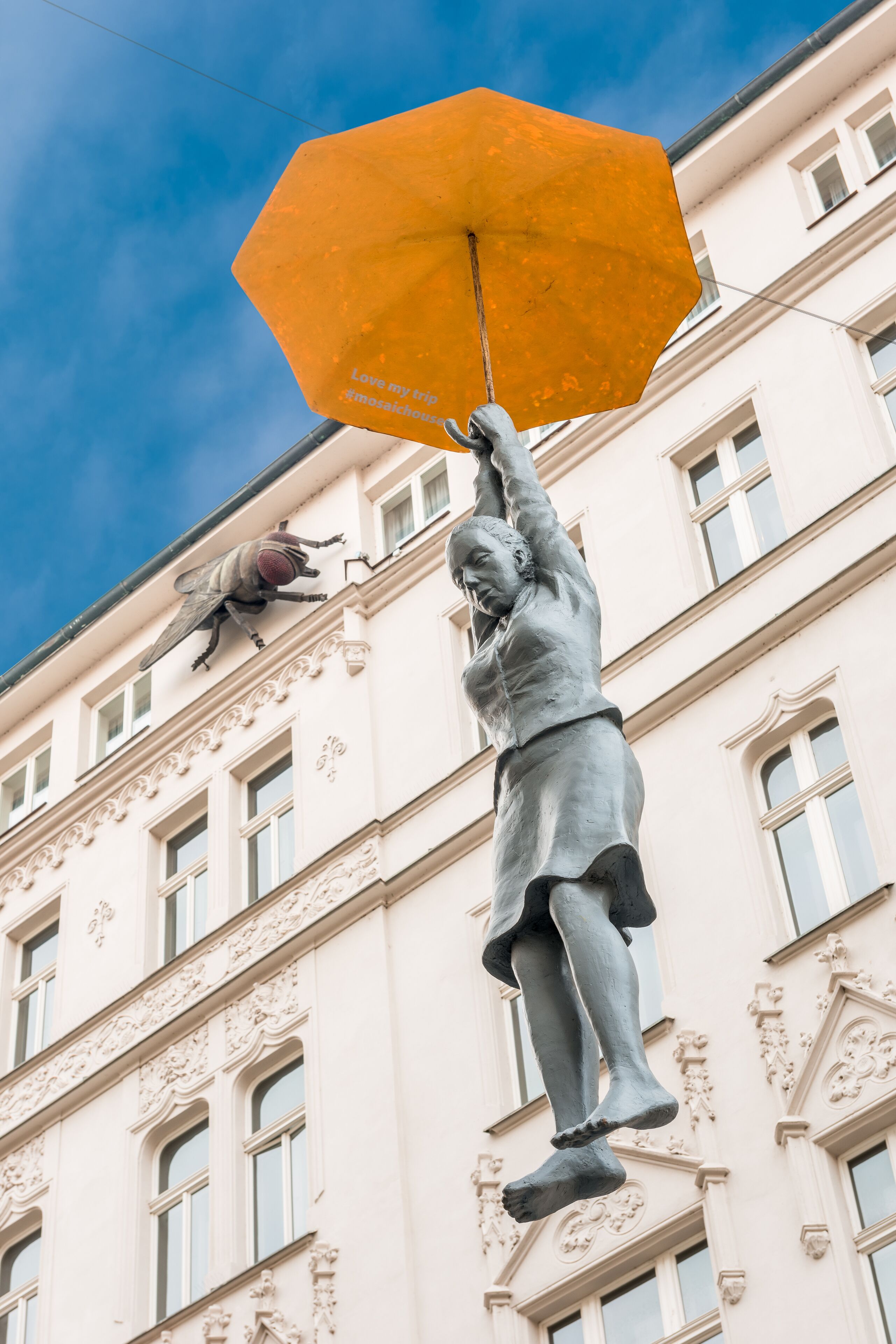 A statue of a person holding an umbrella in front of a building with ornate architectural details.