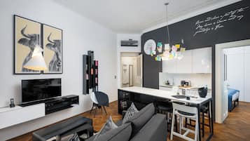 Una sala de estar moderna con sofá, televisor y obras de arte. Se observa un área de cocina con una mesa de comedor y sillas.