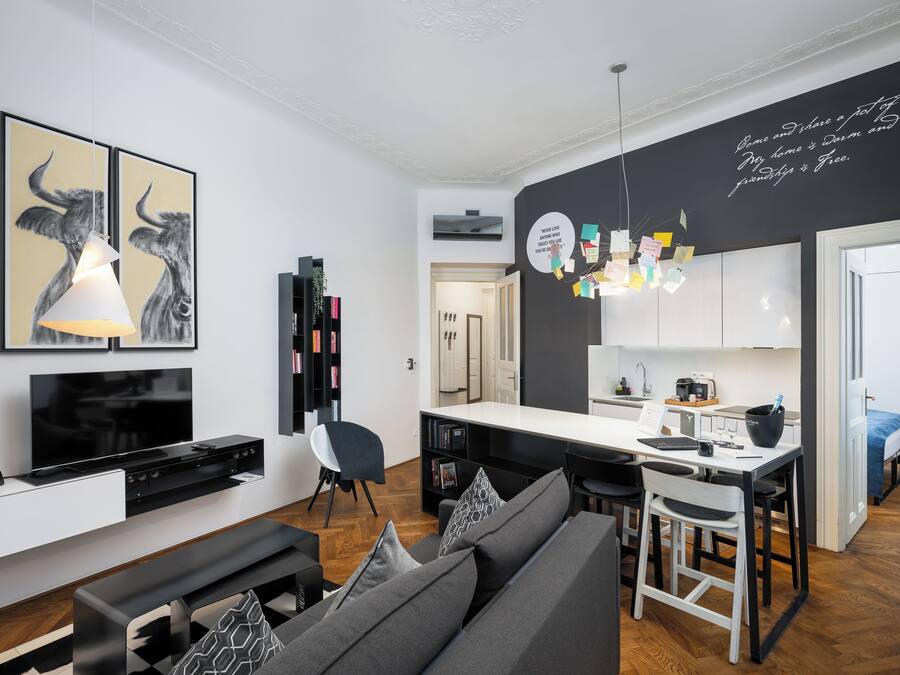 Una sala de estar moderna con sofá, televisor y obras de arte. Se observa un área de cocina con una mesa de comedor y sillas.