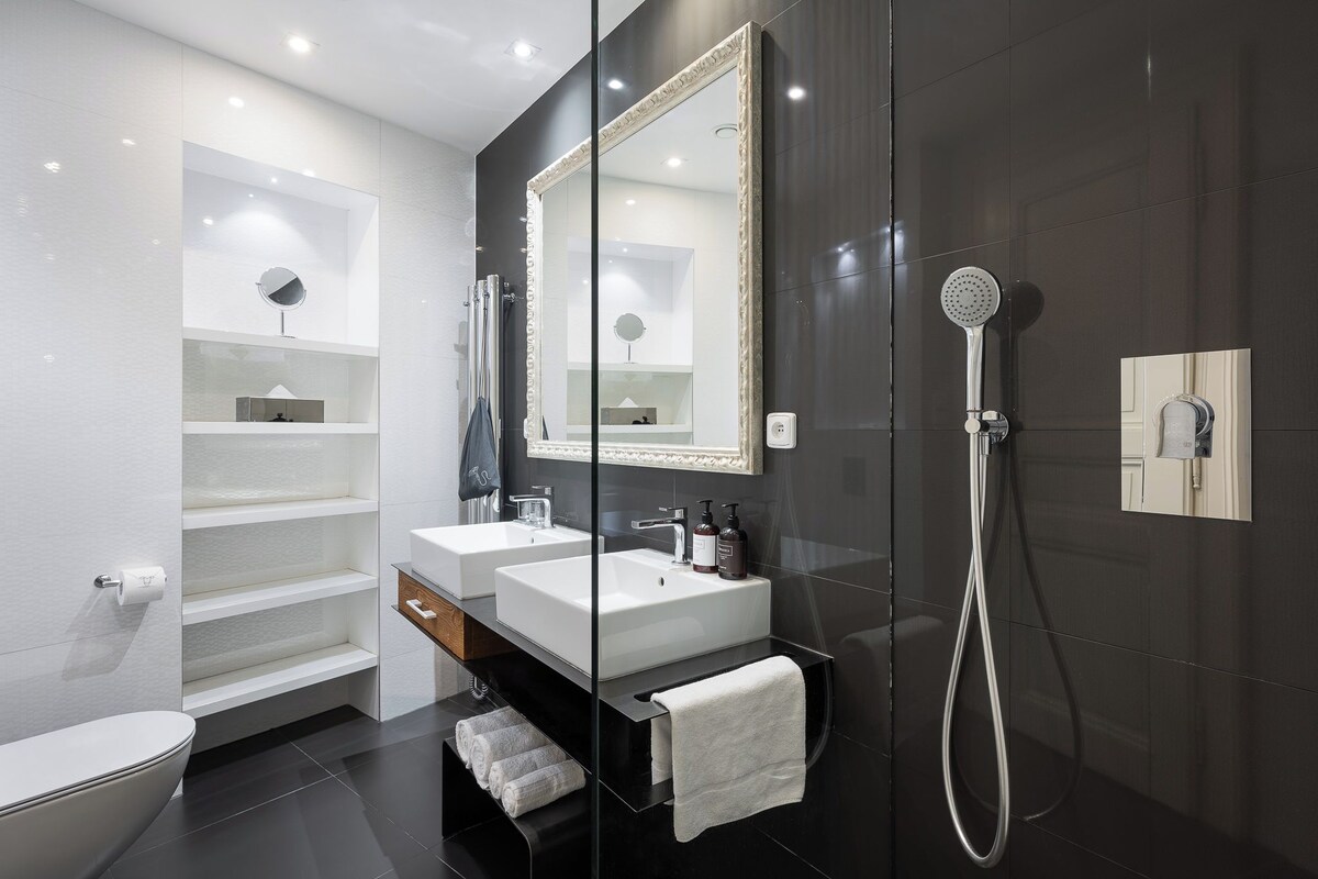 Un baño moderno con ducha acristalada, dos lavamanos y un espejo grande.