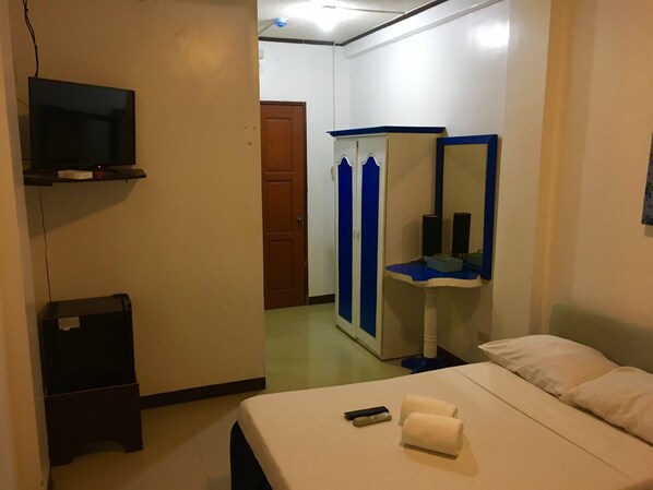 Habitación de hotel con cama, mesita de noche, espejo, armario y televisor montado en la pared.