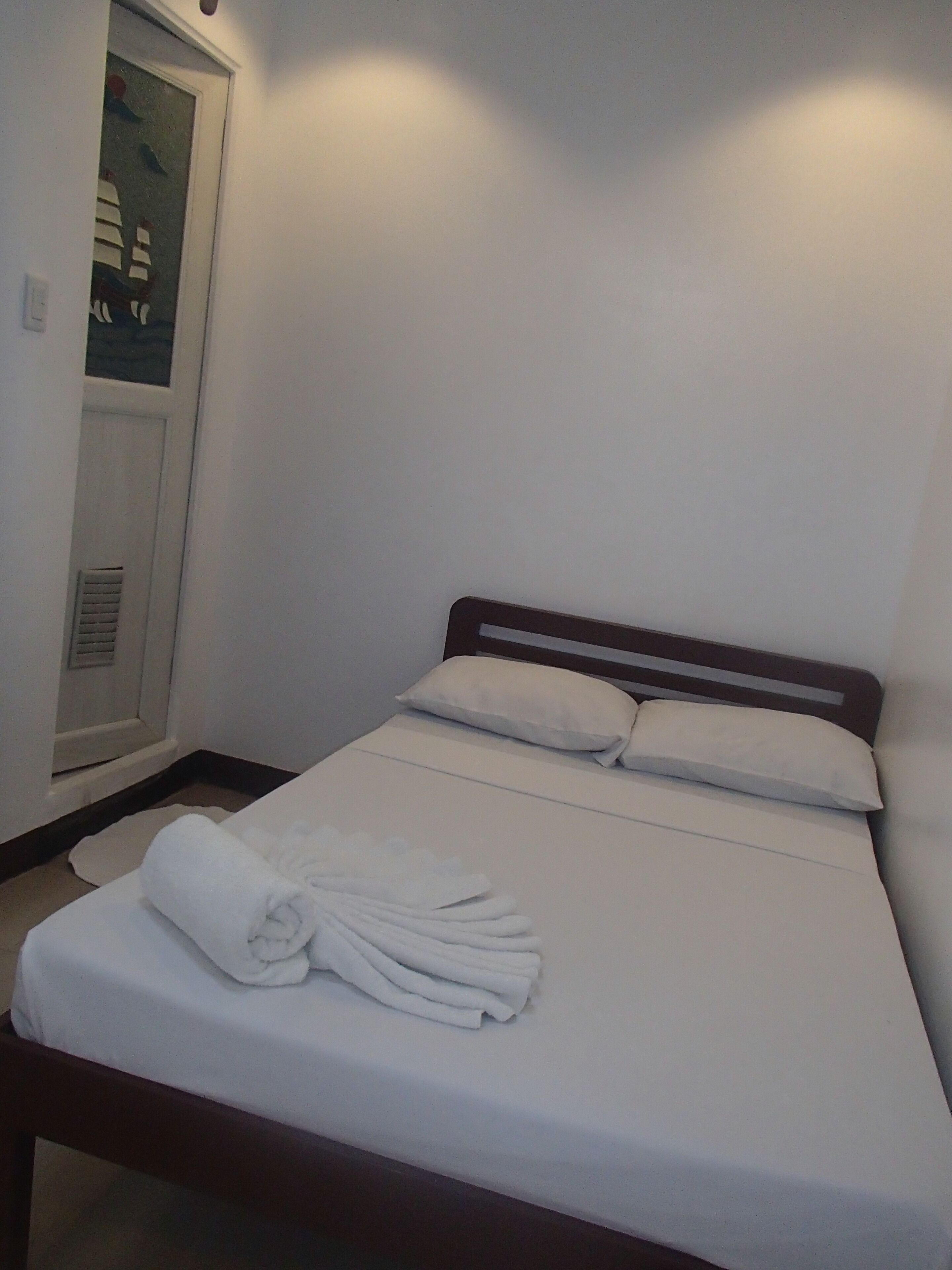 A neatly made bed with white linens and pillows, a wooden headboard, and a white towel folded on the bed.