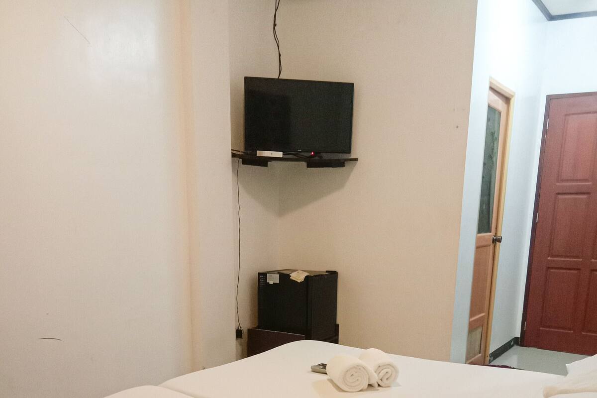 Ein Hotelzimmer mit zwei Betten, jeweils mit ordentlich aufgerollten Handtüchern. Ein Fernseher ist an der Wand über den Betten angebracht.