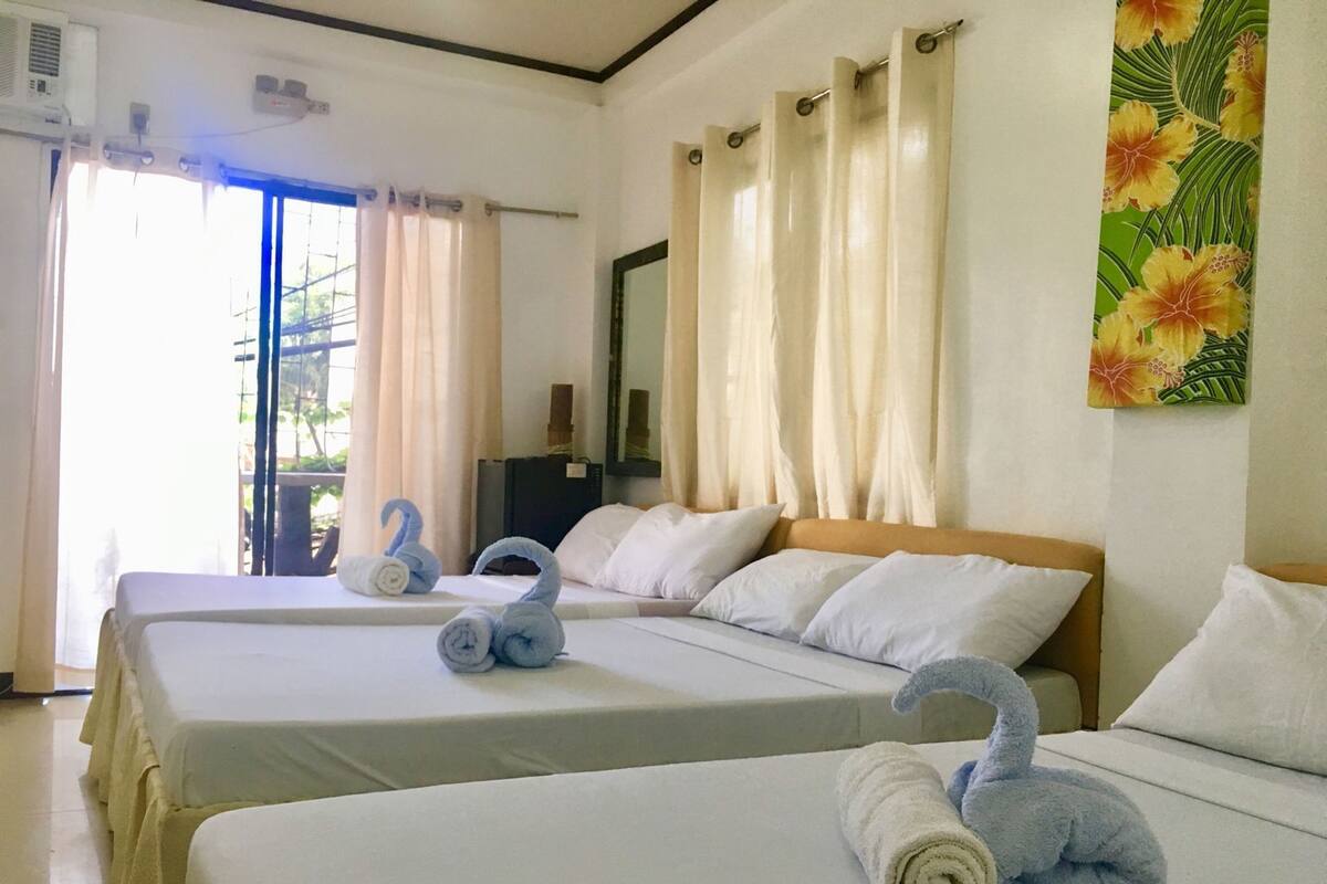 Ein Hotelzimmer mit zwei Betten, einem großen Fenster mit Vorhängen, einer Wandklimaanlage und einem Gemälde.