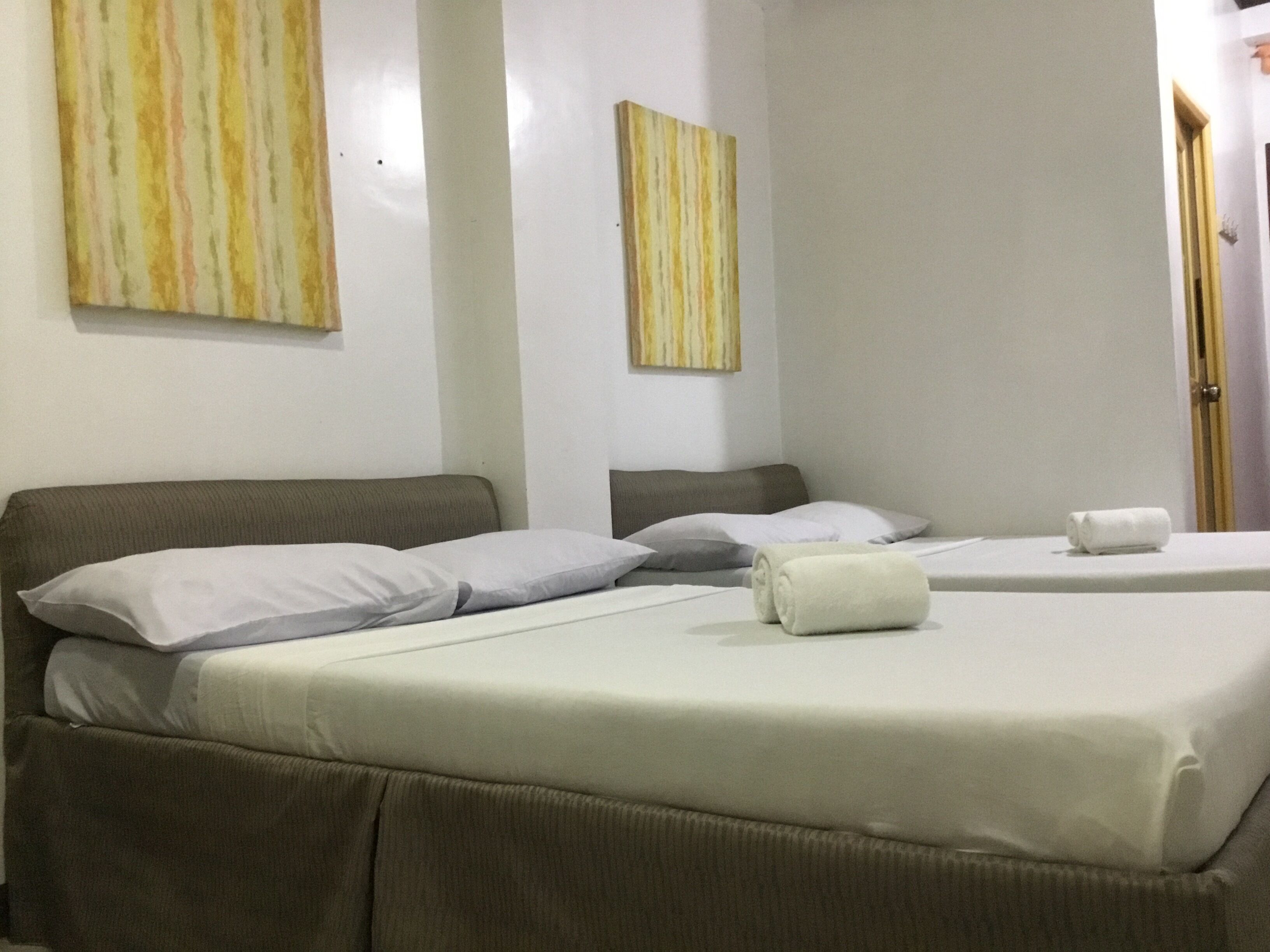 A hotel room with two beds, each with a pillow and a rolled towel.