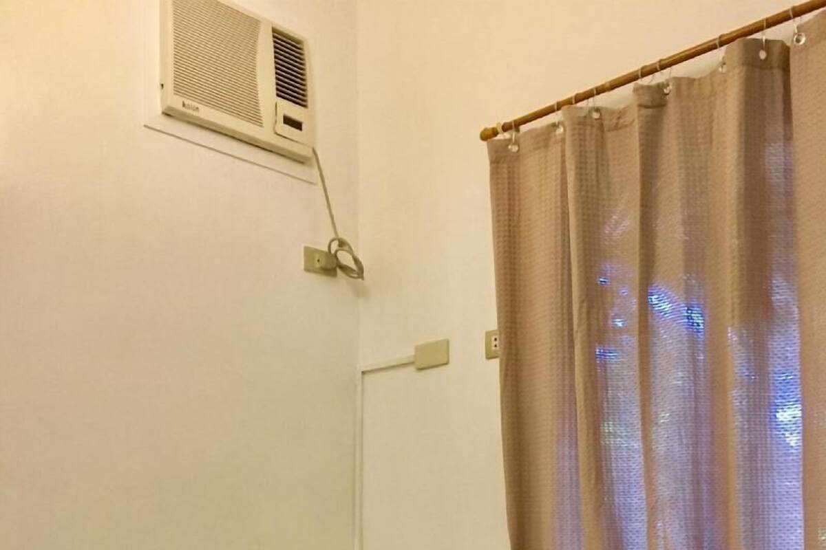 Ein Einzelbett mit Kissen und zusammengelegtem Handtuch, einer Fernbedienung, einer Wand-Klimaanlage und einem Vorhang.