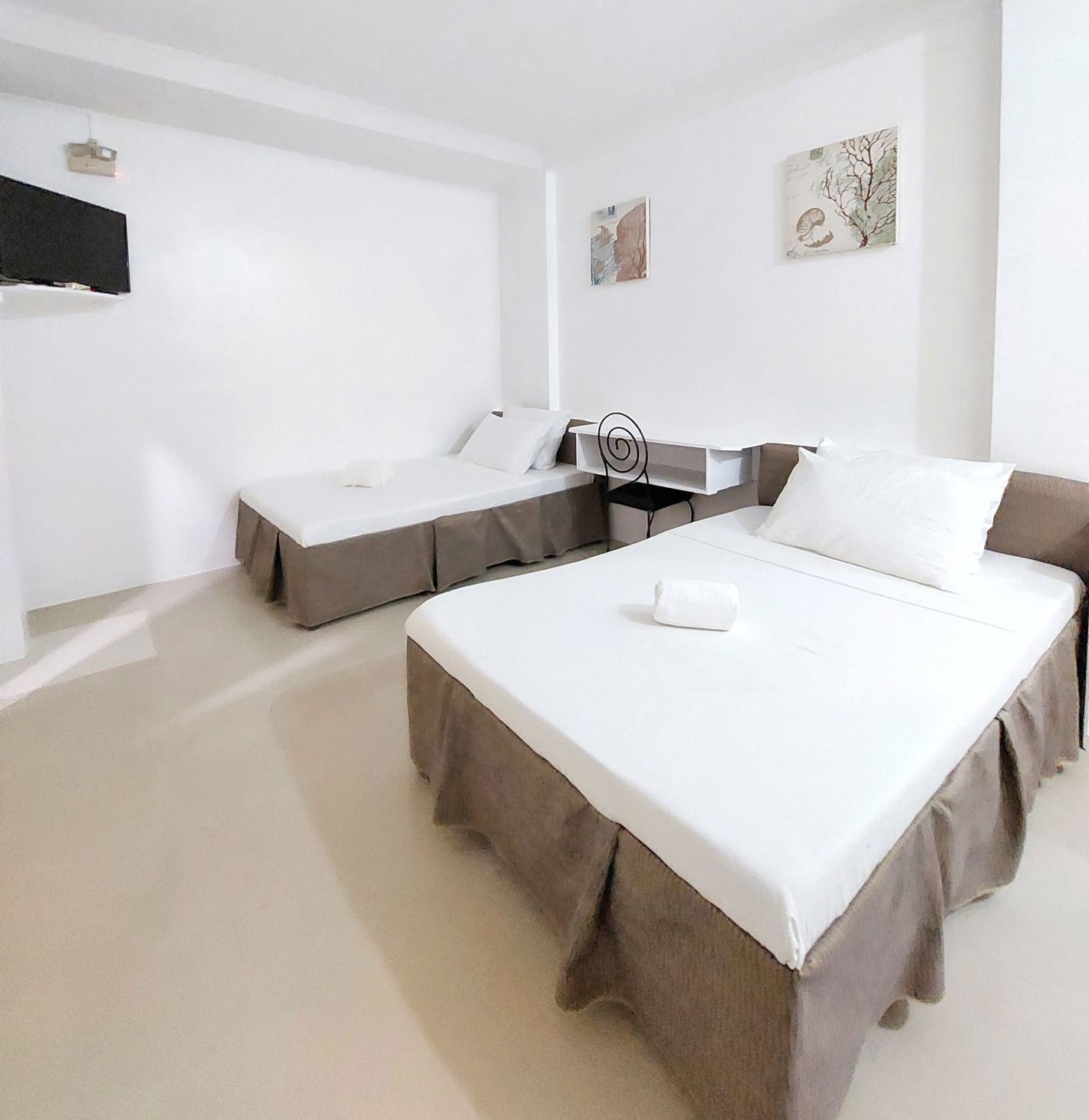 A hotel room with two beds, a desk, and artwork on the walls.