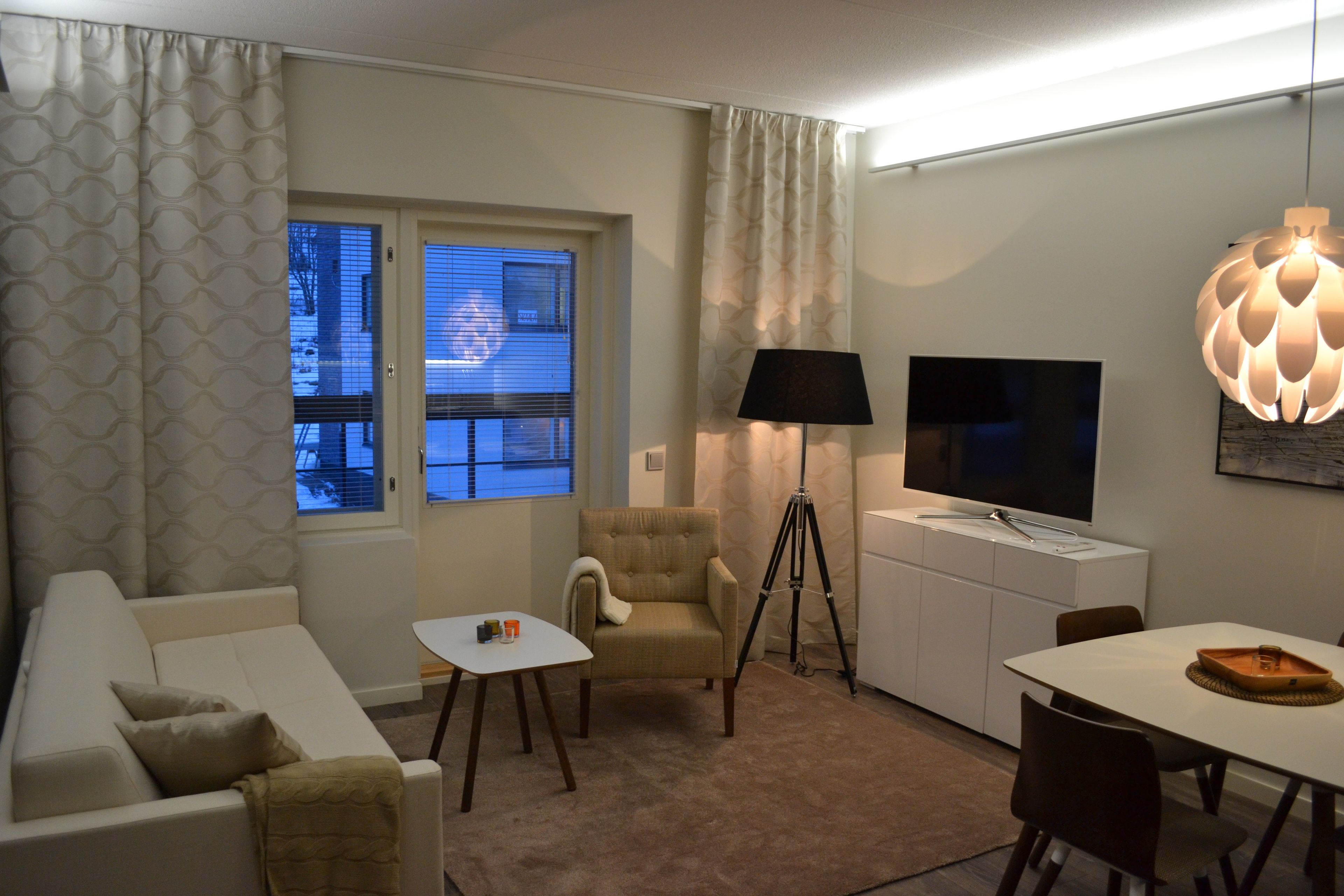 Una sala de estar con sofá, sillón, mesa de comedor y televisor sobre un mueble.