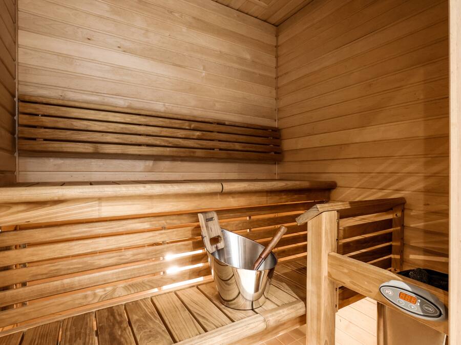 Een sauna met houten banken en een metalen emmer met een houten hamer.