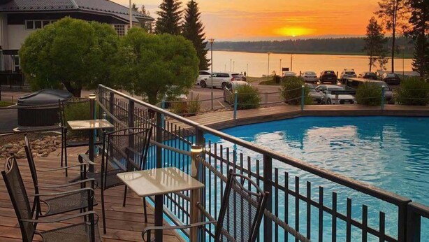 Zona de piscina con vista al atardecer, mobiliario exterior y un edificio al fondo.