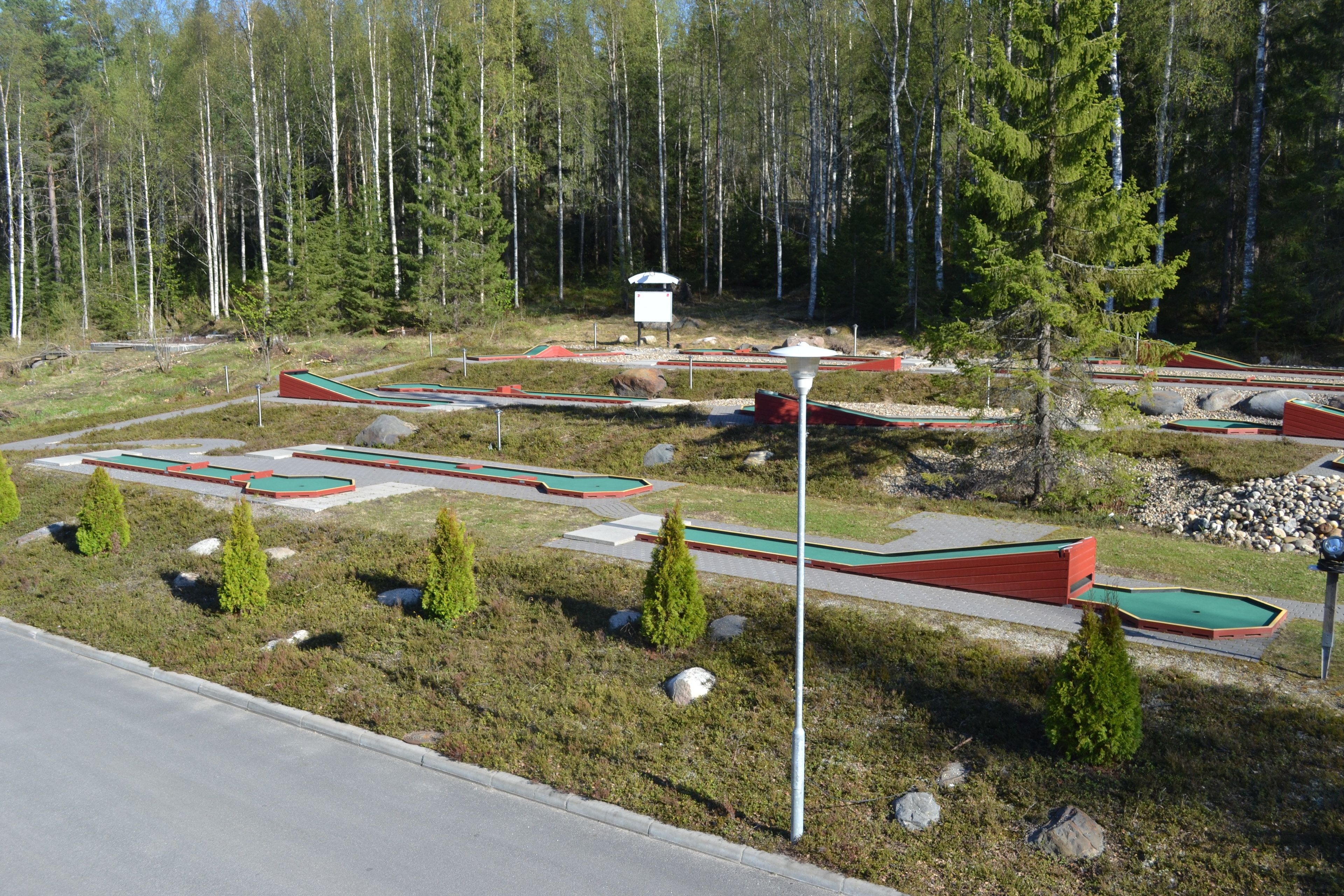 A miniature golf course with multiple green and red holes, surrounded by a forested area.